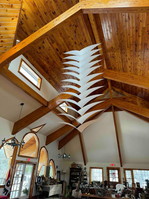 Large pendulum wave sculpture by Bob Hausslein, showcasing intricate design and engineering, displayed in a gallery space