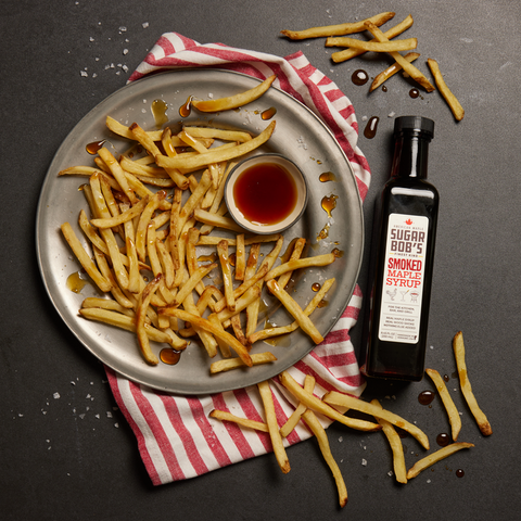 A bottle of Sugar Bob’s Smoked Maple Syrup next to a bowl of French fries 