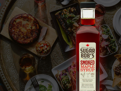 Bottle of Sugar Bob’s Smoked Maple Syrup next to roasted vegetables and hardwood smoke