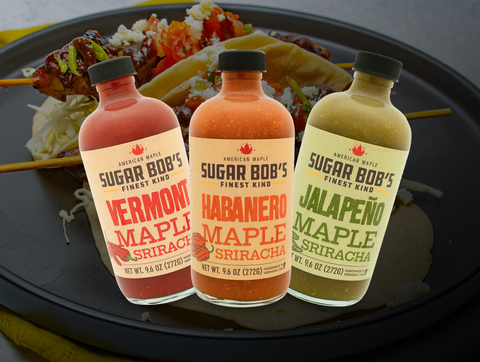 Three bottles of Sugar Bob’s Maple Sriracha — Original, Jalapeño, and Habanero — with fresh peppers and Vermont maple syrup.