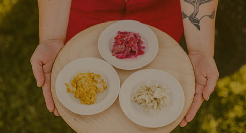 wooden board with three bowls of sauerkraut, kimchi, and pickles