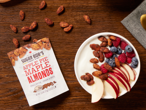 A box of apple pie mapple almonds next to a bowl of yogurt and some fruit 
