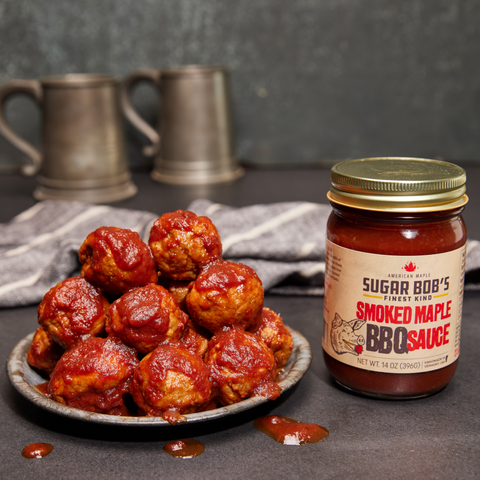 Plate of meatballs and a jar of Smoked Maple BBQ Sauce on a dark surface.